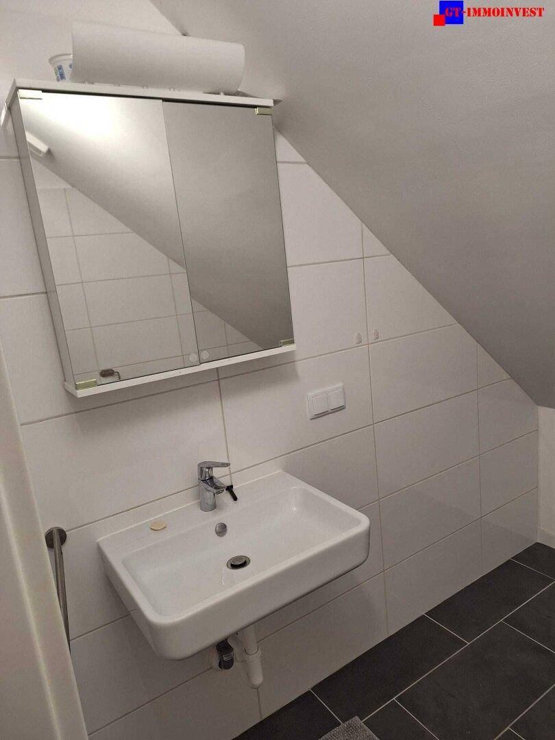 Modernes Badezimmer mit Waschbecken, Spiegelschrank und dunklen Fliesen im Dachgeschoss.
