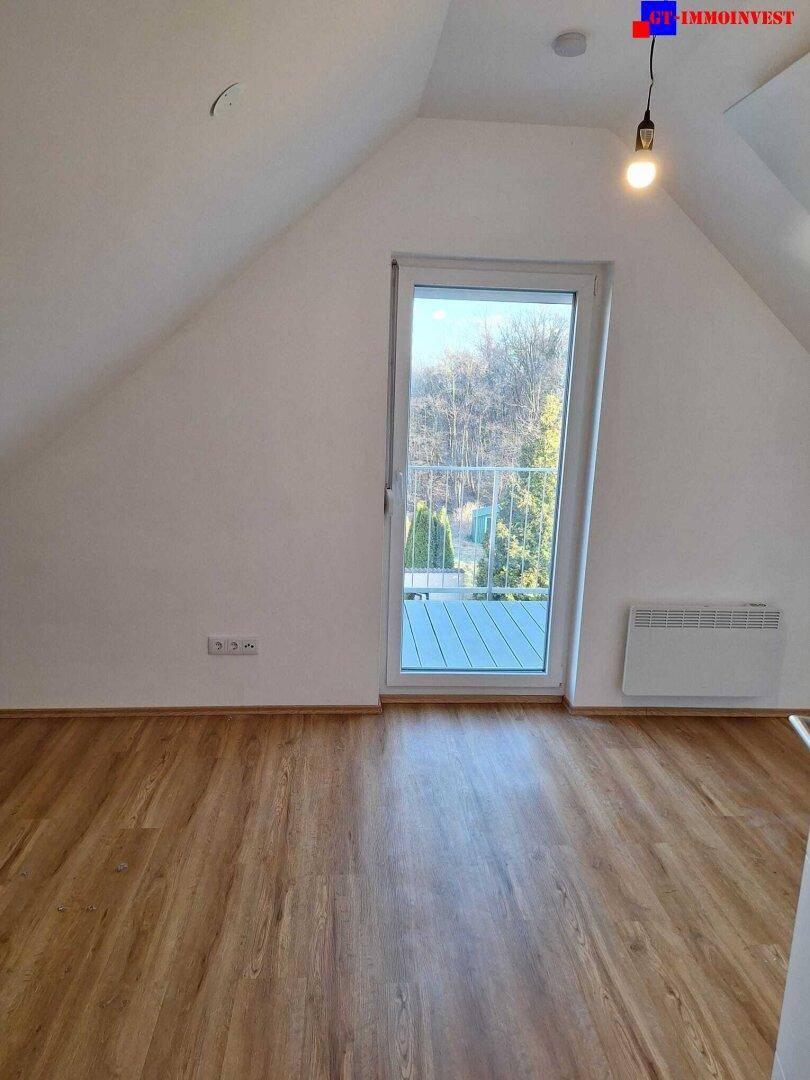 Schlafzimmer im Dachgeschoss mit Zugang zum Balkon und schräger Decke.