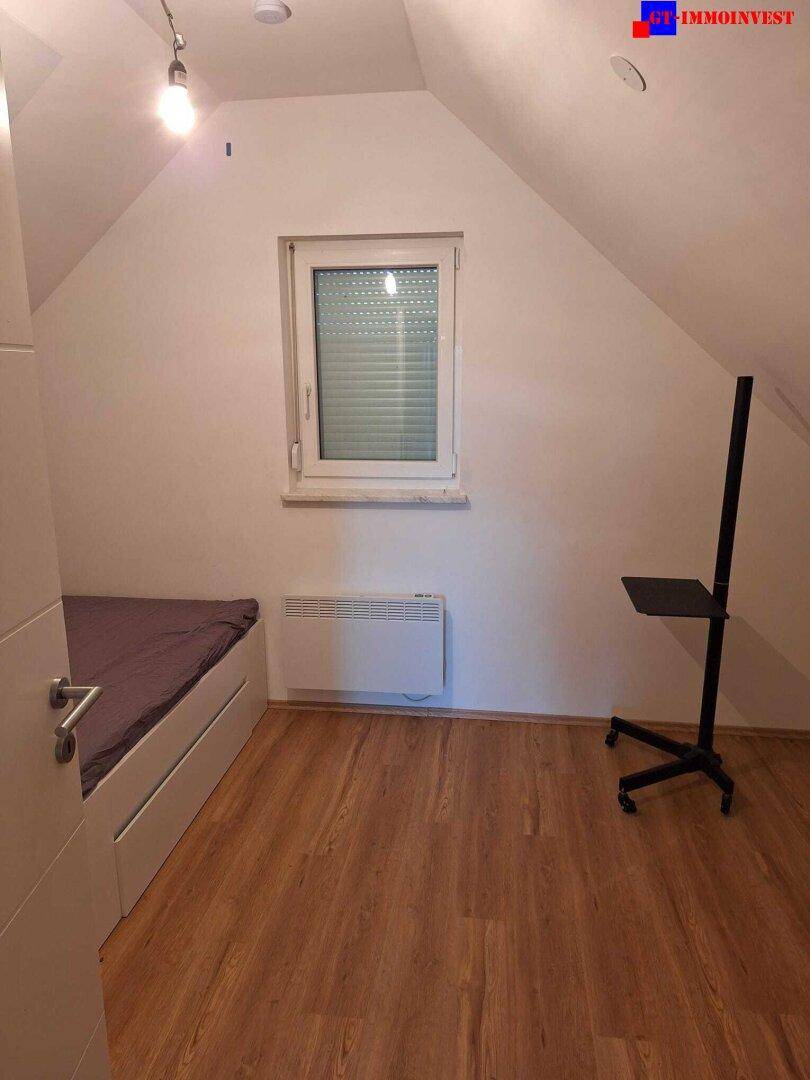 Schlafzimmer im Dachgeschoss mit Laminatboden, Fenster und schräger Decke.