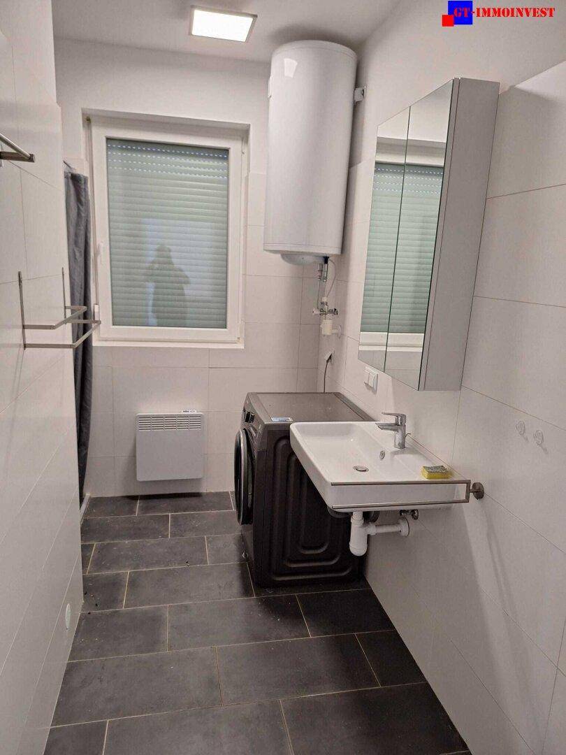 Badezimmer mit Fenster, Waschmaschine, Waschbecken und Spiegelschrank.