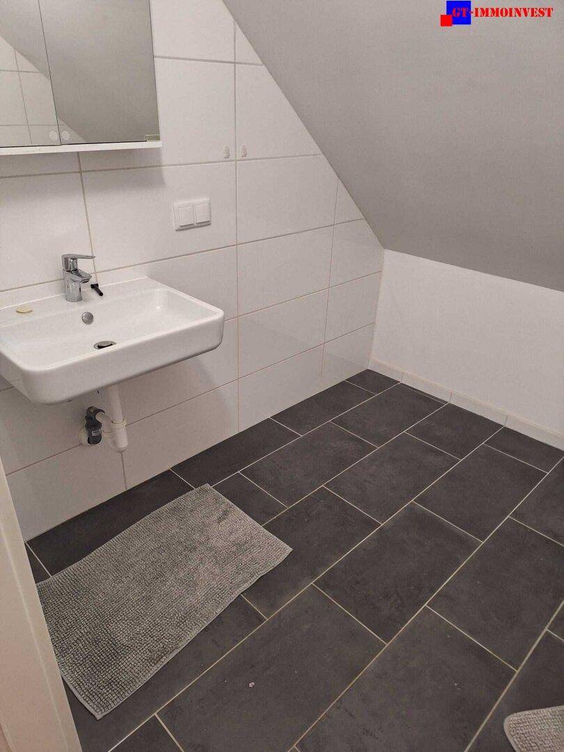 Modernes Badezimmer mit Waschbecken, Spiegelschrank und dunklen Fliesen im Dachgeschoss.