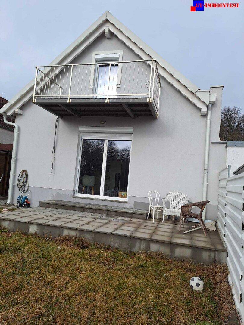 Rückseite des Hauses mit Balkon, gepflasterter Terrasse und kleinem Gartenbereich.