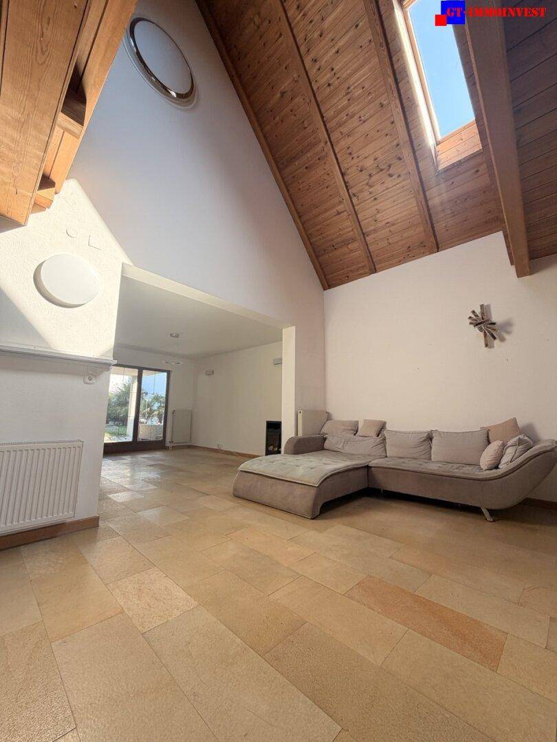 Geräumiges Wohnzimmer mit hohen, gewölbten Holzdecken, Oberlicht und hellem Fliesenboden.