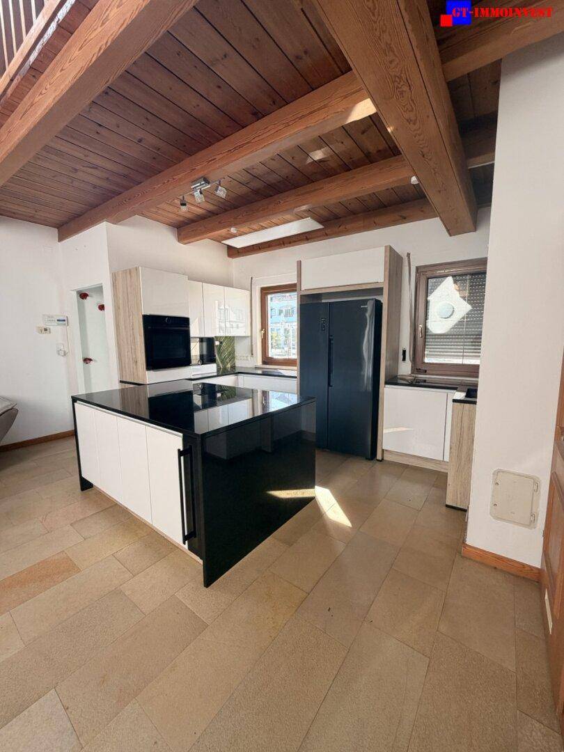 Moderne Küche mit Kochinsel, schwarzen Geräten und rustikaler Holzdeckenbalkenkonstruktion.