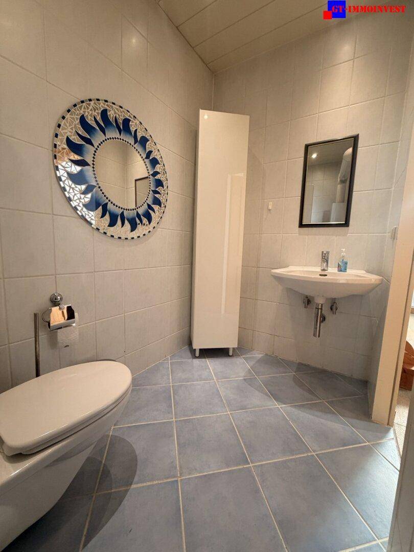Gästetoilette mit blauen Bodenfliesen, wandmontiertem WC und modernem Spiegel.