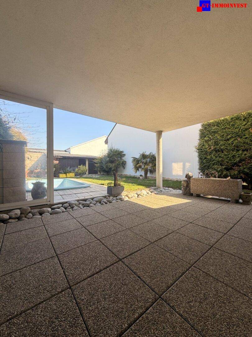 Überdachte Terrasse mit Fliesenboden und Blick auf den Garten sowie den Swimmingpool.