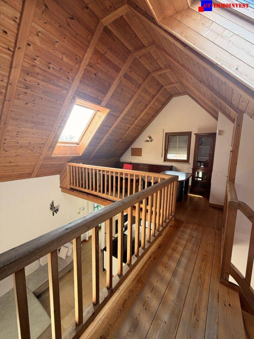 Offener Bürobereich im Obergeschoss mit Holzboden, schrägen Holzdecken und Dachfenster.