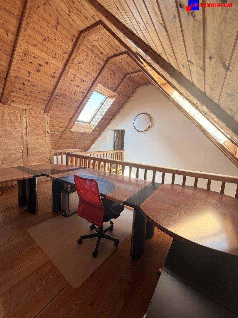 Heller Bürobereich mit großem Schreibtisch, Holzboden und Dachfenster für viel Tageslicht.