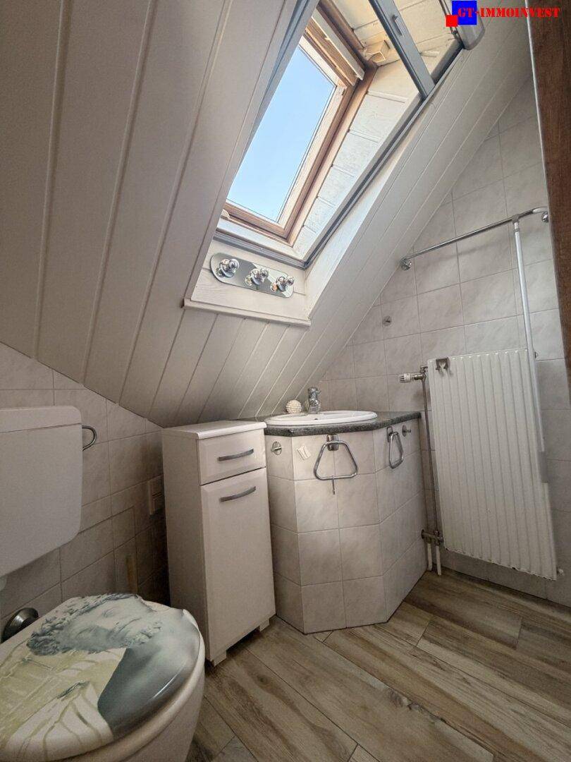 Badezimmer im Dachgeschoss mit Dachfenster, WC, Waschbecken und schrägen Wänden.