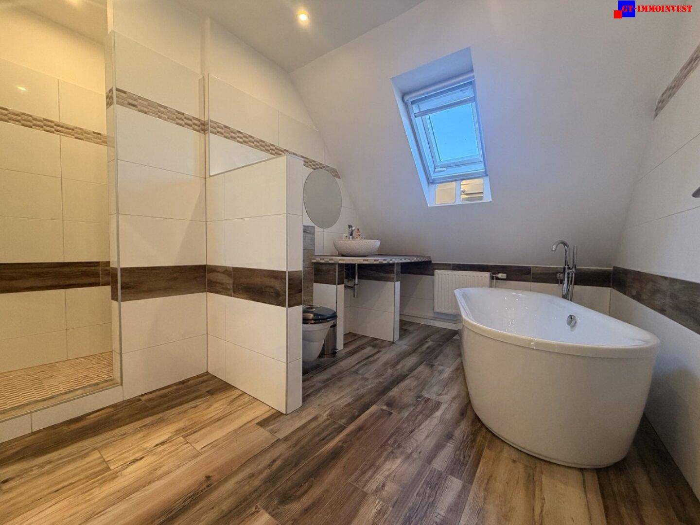 Geräumiges Badezimmer mit freistehender Badewanne, Duschbereich und Dachfenster.