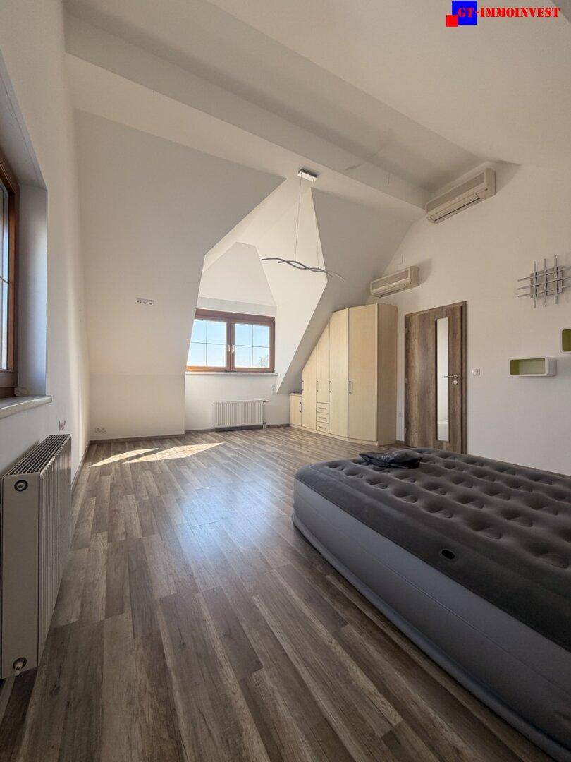 Helles Schlafzimmer mit Laminatboden, Dachschrägen und Fenster mit Blick nach draußen.