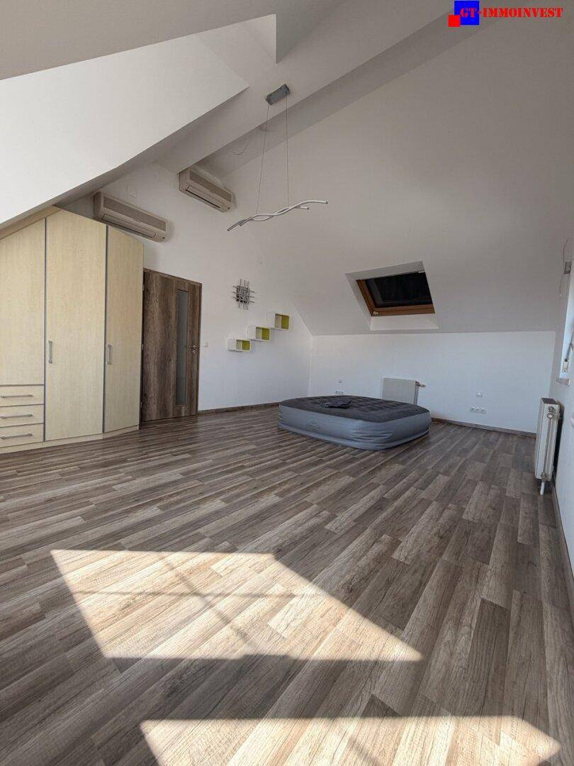 Geräumiges Schlafzimmer im Dachgeschoss mit Laminatboden, Dachschrägen und Klimaanlage.