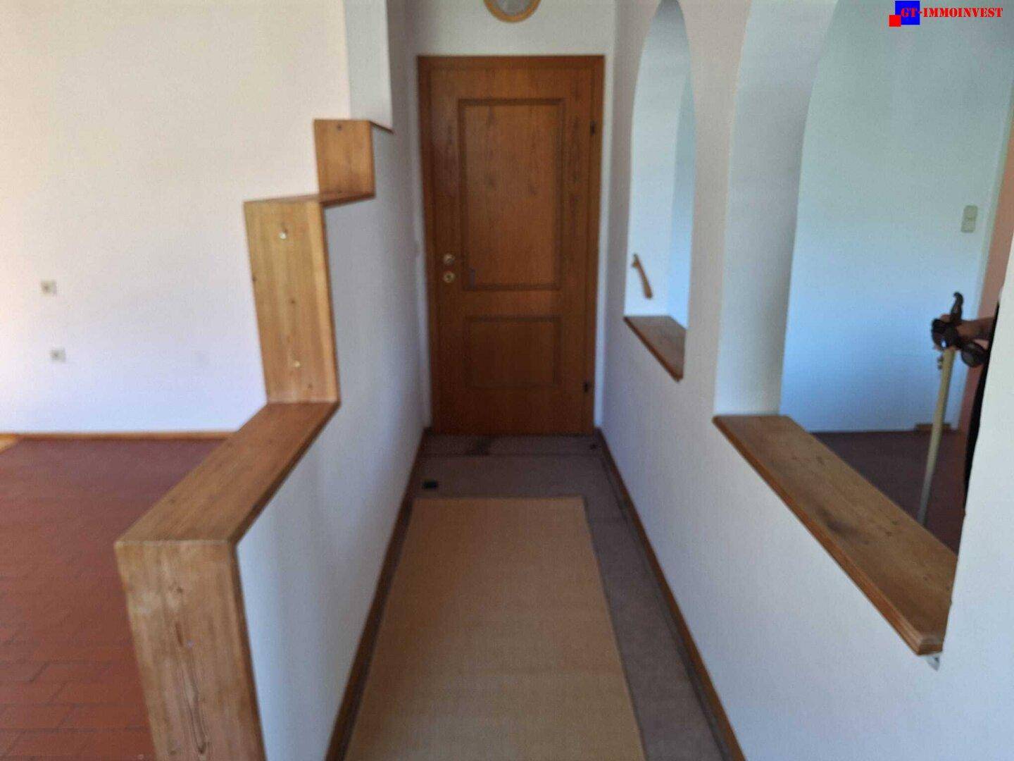 Eingangsbereich mit Holztür, Holztreppe und gefliestem Boden.
