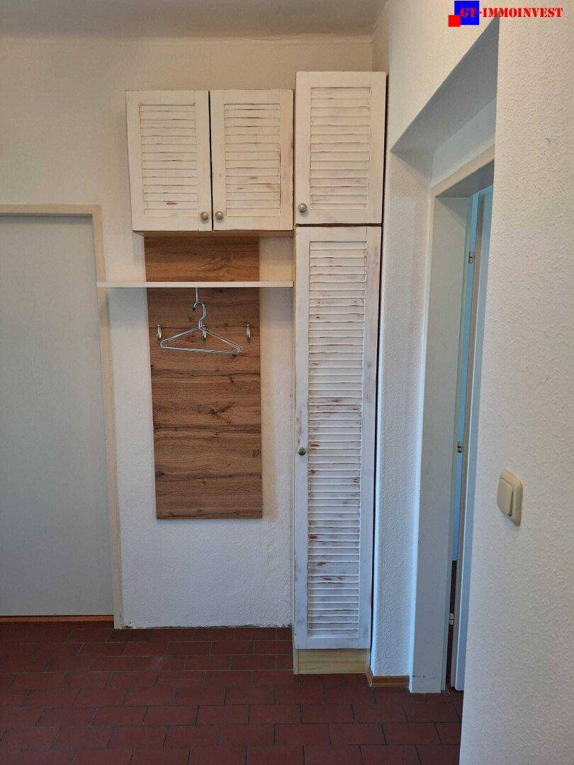 Flur mit weiß gestrichenen Wänden, Garderobe und Schränken mit Lamellentüren.