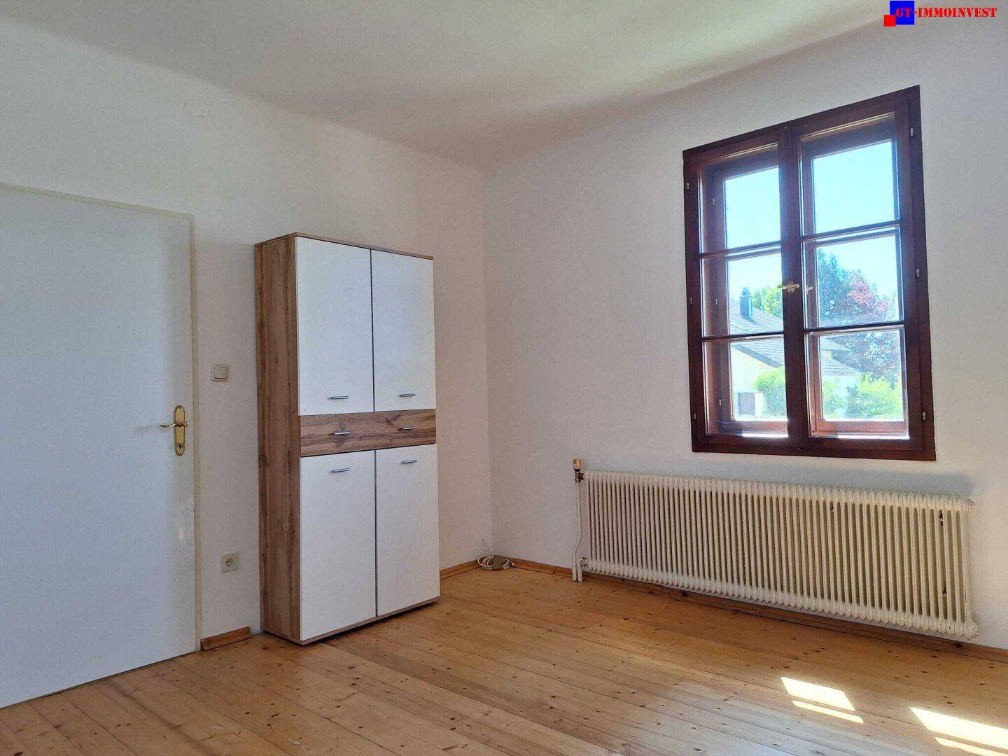 Helles Schlafzimmer mit Holzboden, einem Fenster und einem Kleiderschrank.