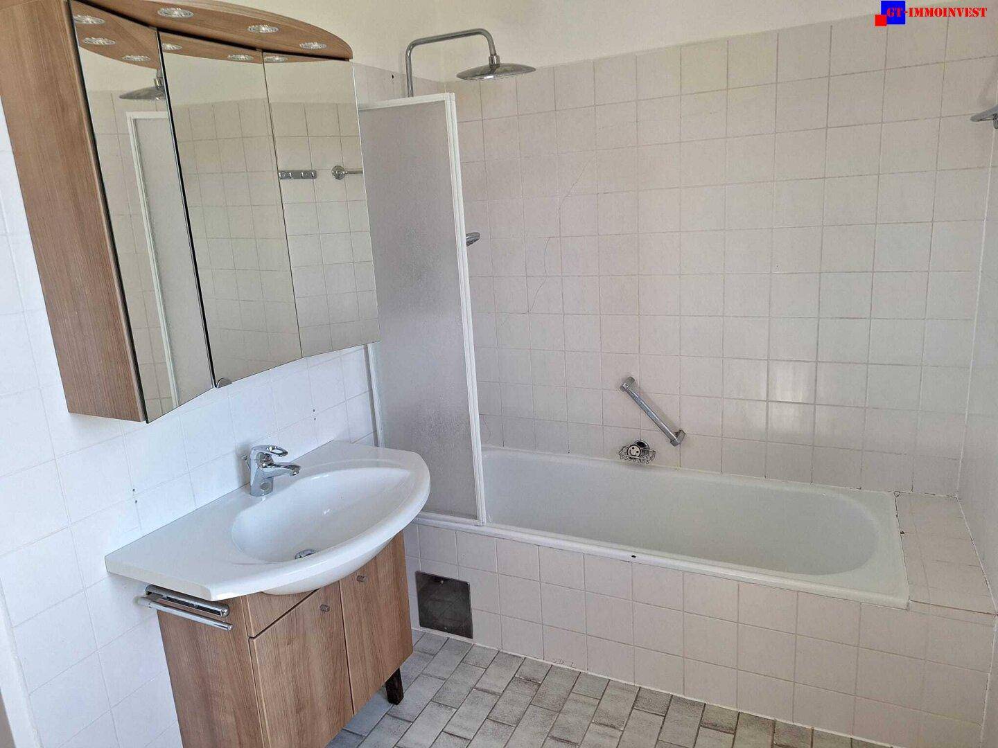 Badezimmer mit weißen Fliesen, Badewanne, Duschvorrichtung und Waschbecken mit Spiegelschrank.