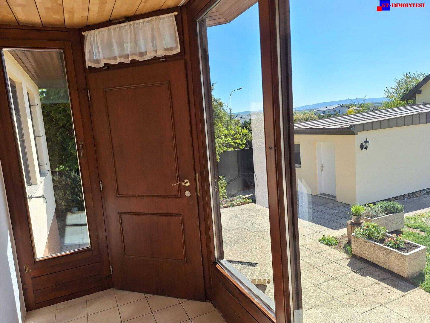 Heller Eingangsbereich mit großen Glasflächen, Holztür und Blick auf den Außenbereich.