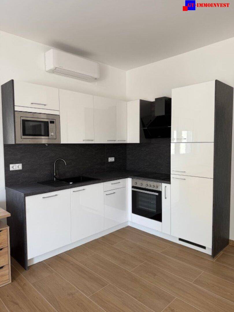 Moderne Einbauküche mit weißen Hochglanzfronten, dunkler Arbeitsplatte und integrierten Geräten.
