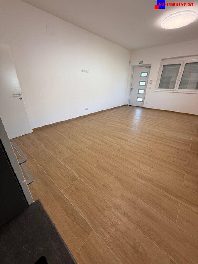 Geräumiger, heller Raum mit modernem Fliesenboden in Holzoptik und Zugang zu weiteren Bereichen.