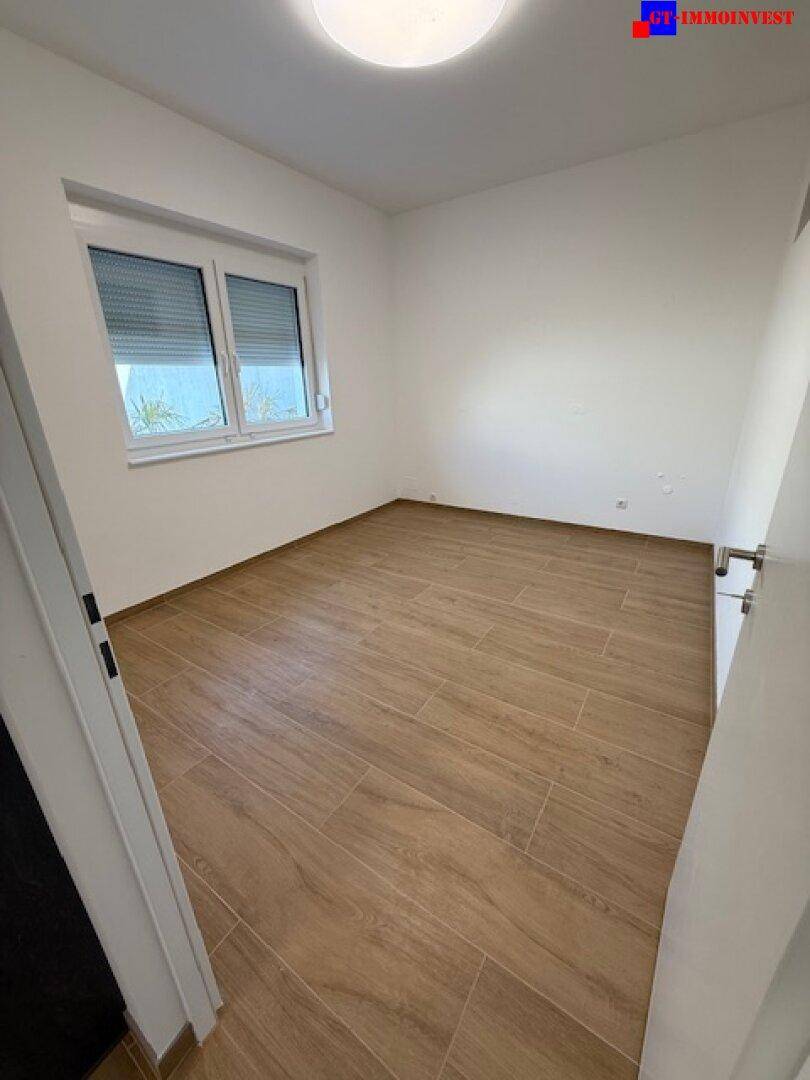 Helles Schlafzimmer mit Fliesenboden in Holzoptik und einem Fenster mit Rollladen.