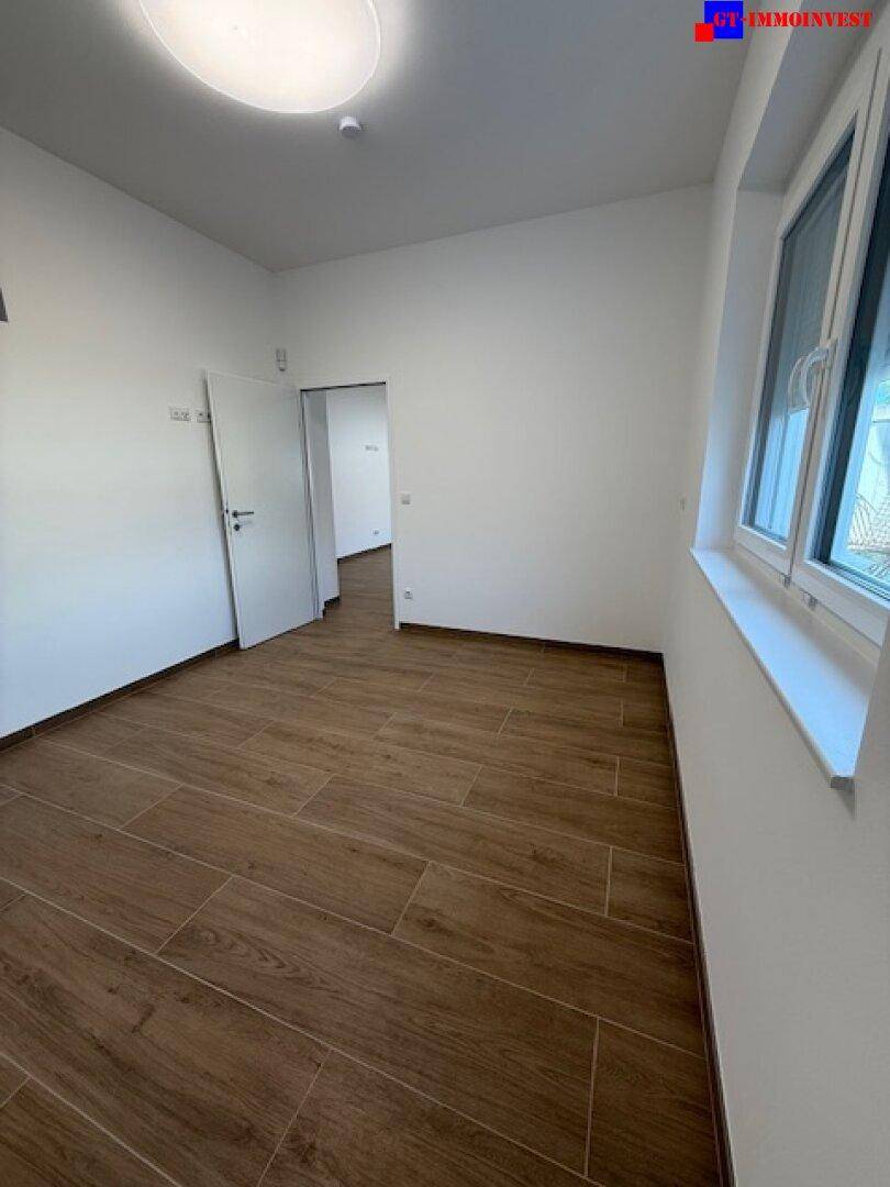 Freundliches Zimmer mit Fliesenboden in Holzoptik und weiß gestrichenen Wänden, ideal als Schlafzimmer.