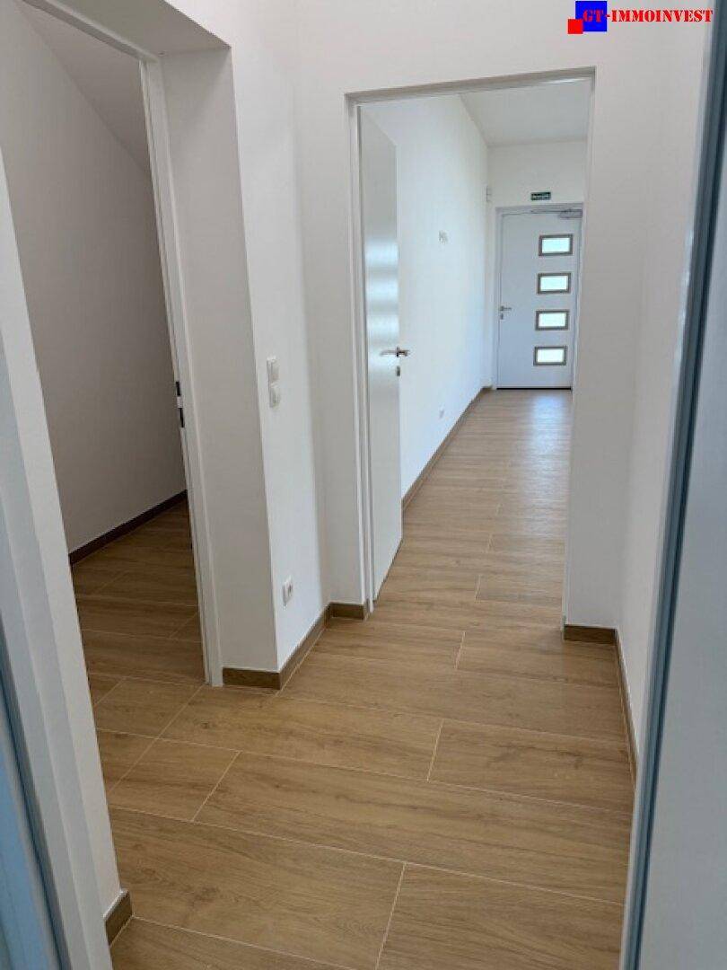 Langer, heller Flur mit Fliesenboden in Holzoptik und mehreren Türen zu den Zimmern.