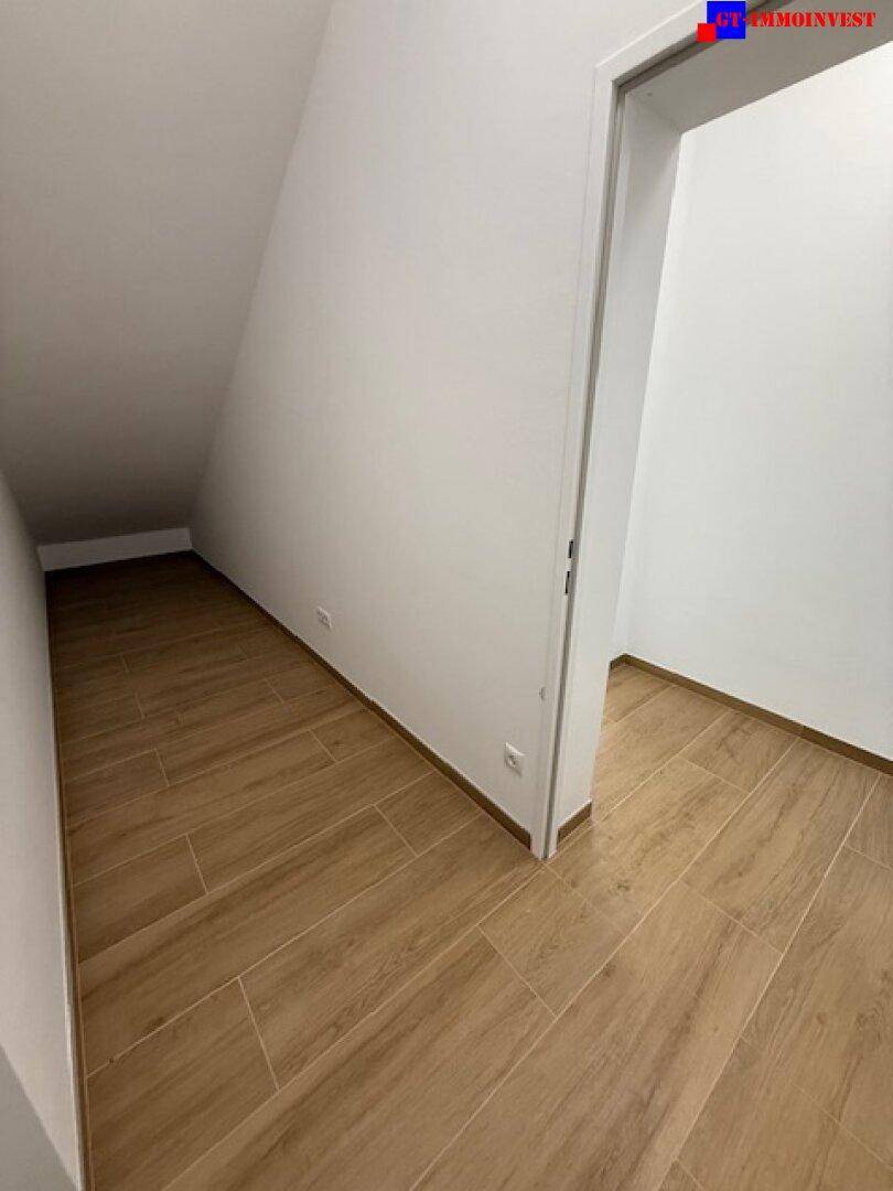 Praktischer Abstellraum mit schräger Decke und Fliesenboden in Holzoptik.