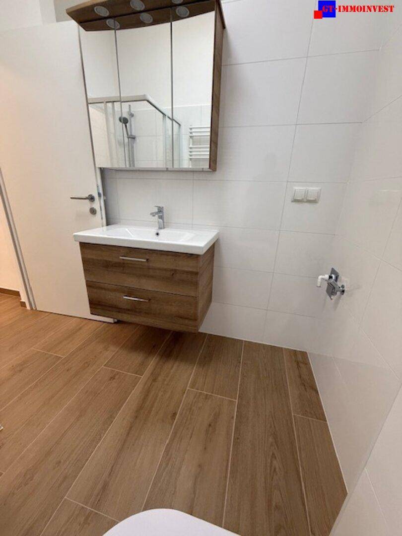 Helles Badezimmer mit modernem Waschtisch, Spiegelschrank und weißen Wandfliesen.