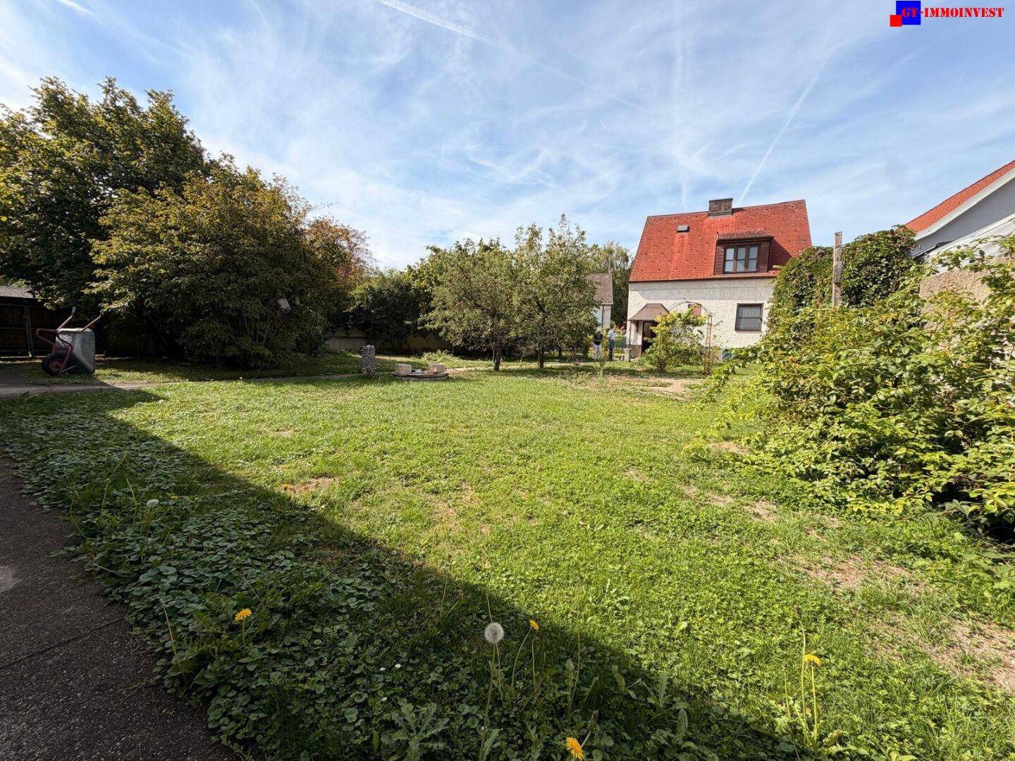 Großer Gartenbereich mit Rasenfläche und Bäumen, das Haus ist im Hintergrund sichtbar.