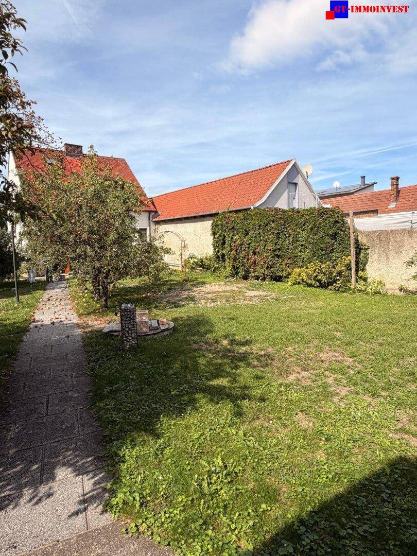 Weitläufige Rasenfläche im Garten mit einer hohen Hecke und dem Haupthaus im Hintergrund.