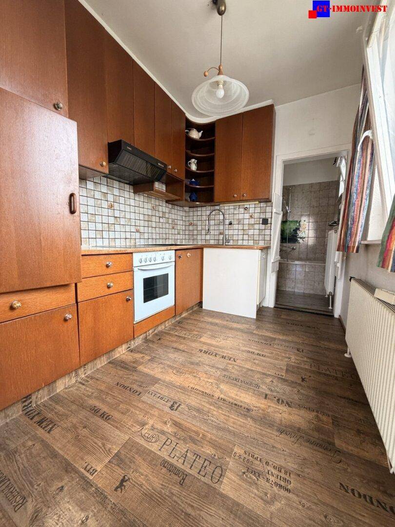 Küche mit braunen Holzschränken, Fliesenrückwand und einem Backofen, daneben ein Durchgang.