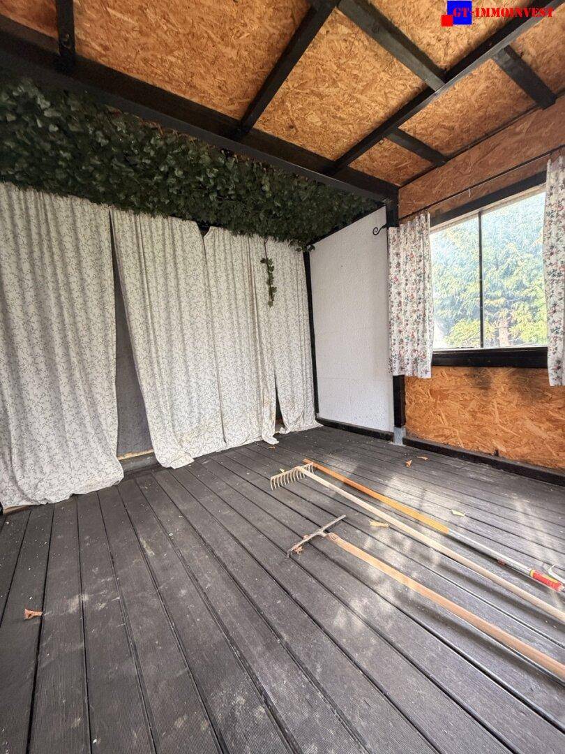 Innenansicht eines Holzschuppens mit dunklem Boden und einem Fenster, Gartengeräte liegen bereit.