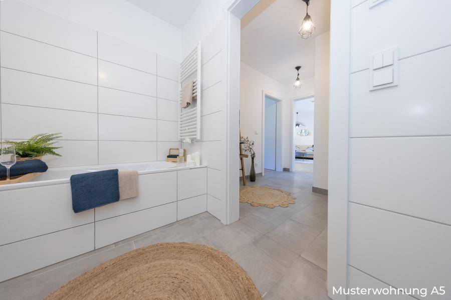 Modernes Badezimmer mit Badewanne, weißen Fliesen und Handtuchheizkörper.