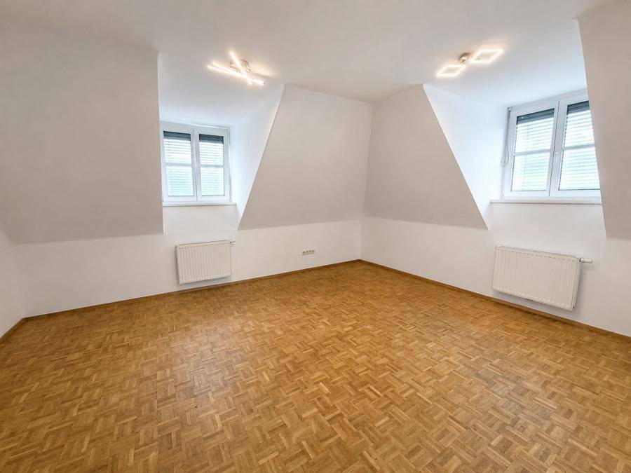 Geräumiges Dachzimmer mit zwei Fenstern, Parkettboden und Heizkörpern, bietet vielseitige Nutzungsmöglichkeiten.