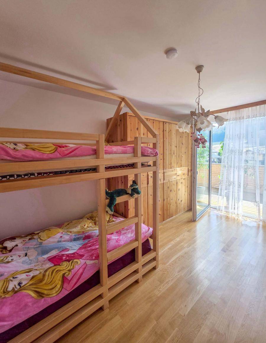 Kinderzimmer mit Etagenbett aus Holz, hellem Parkettboden und Zugang zum Balkon.