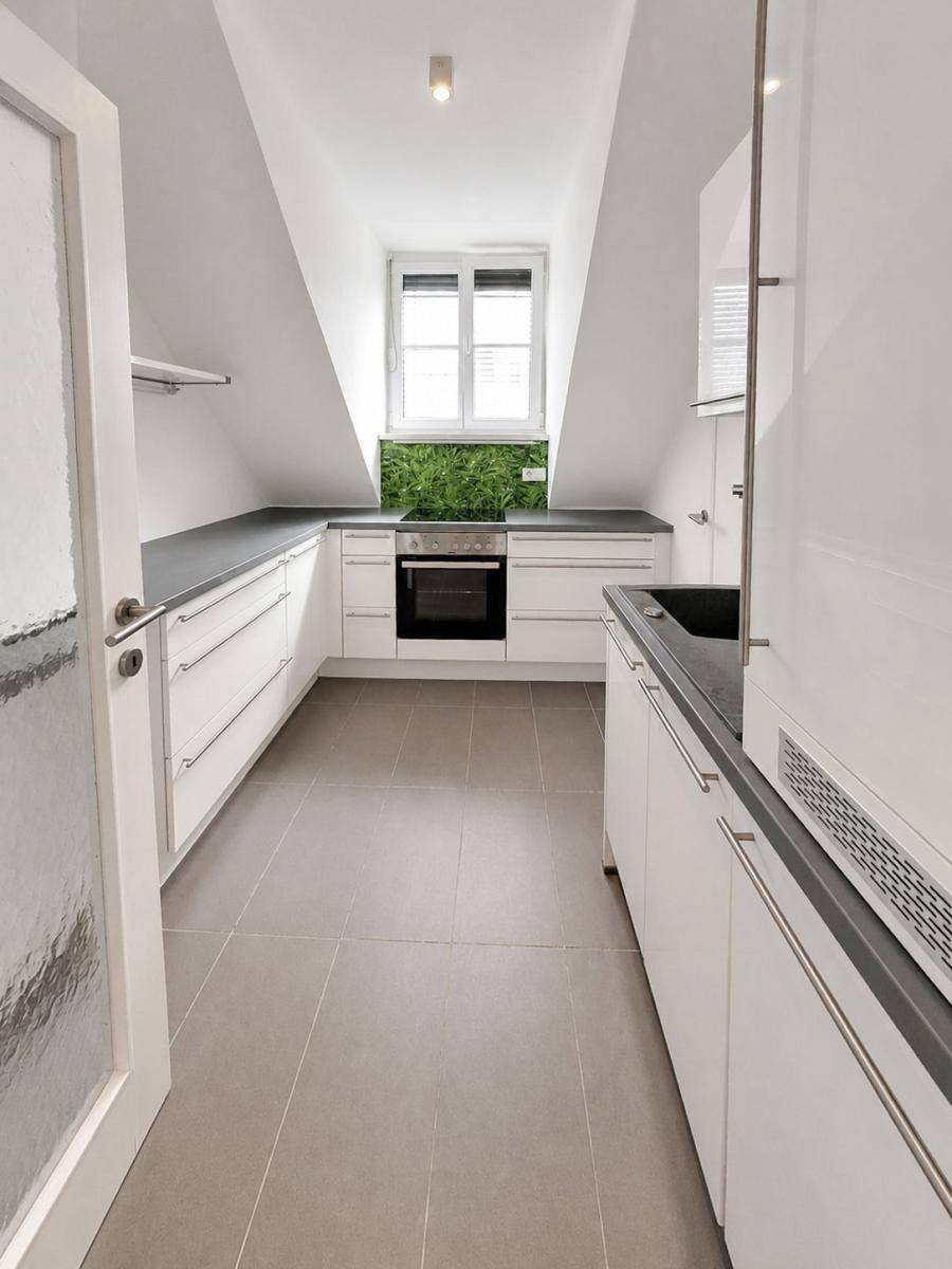 Moderne Küchenzeile im Dachgeschoss mit weißen Schränken, dunkler Arbeitsplatte und grüner Rückwand.