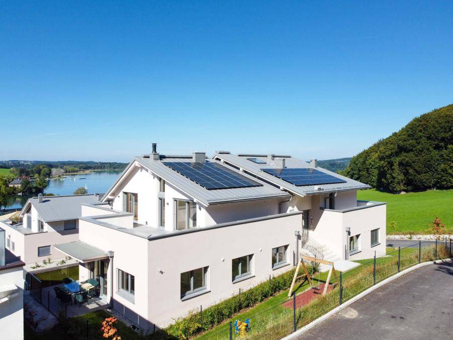 Moderne Wohnanlage mit Solaranlagen auf dem Dach, umgeben von Grünflächen und See.