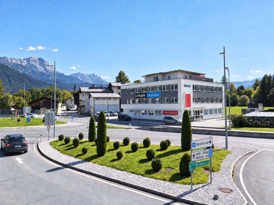 Modernes Bürogebäude an einem Kreisverkehr mit Bergpanorama im Hintergrund unter blauem Himmel.