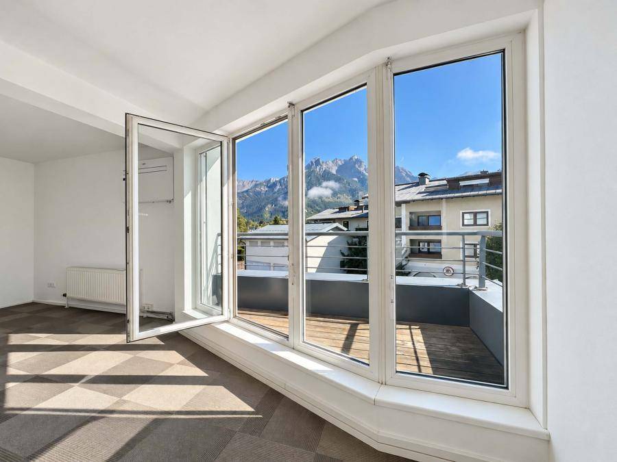Helles Büro mit Teppichboden und großen Fenstern, die Zugang zu einem Balkon und Bergblick bieten.