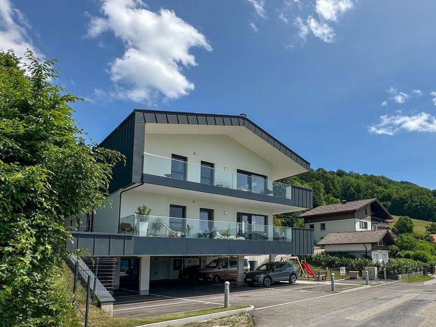 Ansicht des modernen Mehrfamilienhauses mit Balkonen, Carports und einem Spielplatz im Vordergrund.