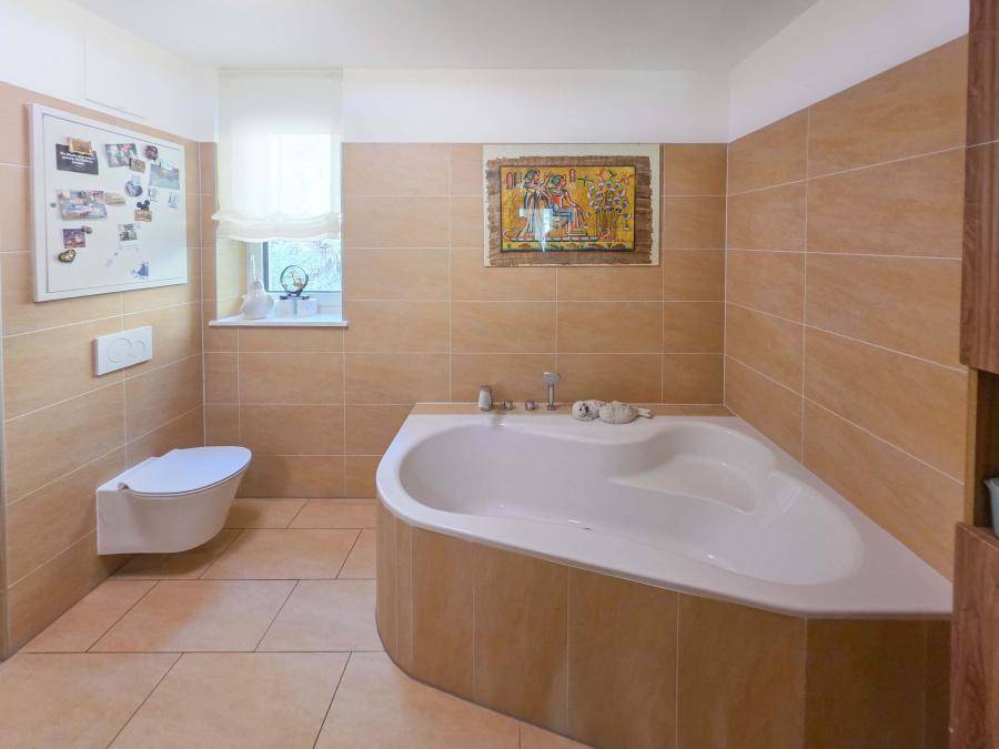 Badezimmer mit beigefarbenen Fliesen, Eckbadewanne und wandhängendem WC.