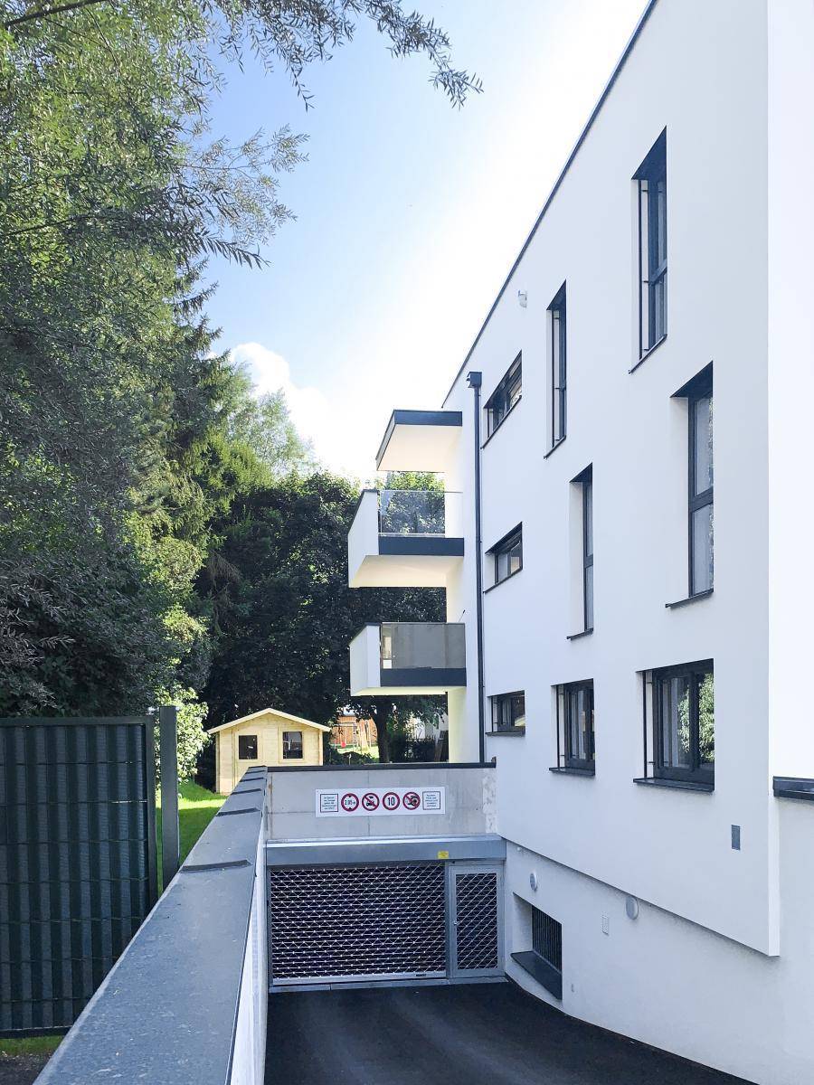 Seitenansicht des modernen Gebäudes mit Zufahrt zur Tiefgarage und umgebendem Grün.