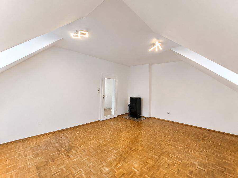 Dachzimmer mit Parkettboden, schrägen Wänden und einem modernen Holzofen für gemütliche Wärme.