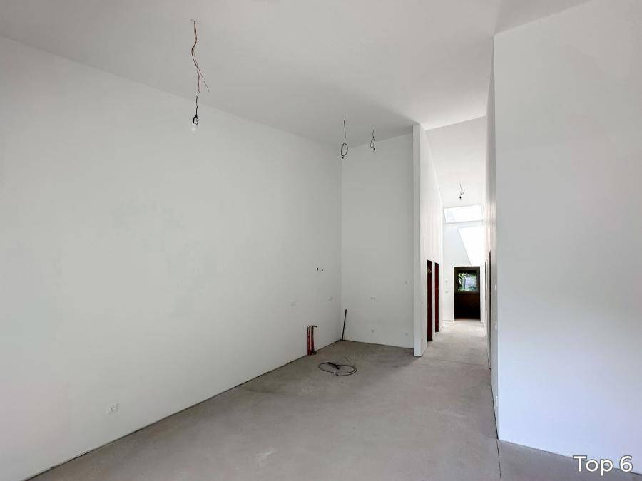 Leerer, heller Raum mit Betonboden und Zugang zu einem Flur, bereit für den Innenausbau.