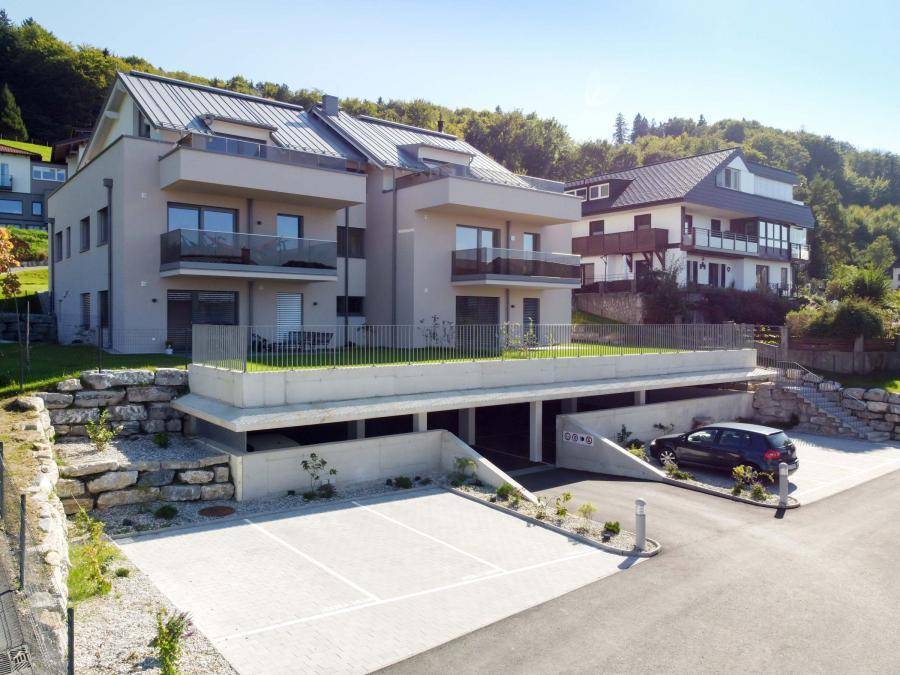Neubauwohnungen mit Balkonen und Tiefgaragenzufahrt, eingebettet in eine grüne Umgebung.