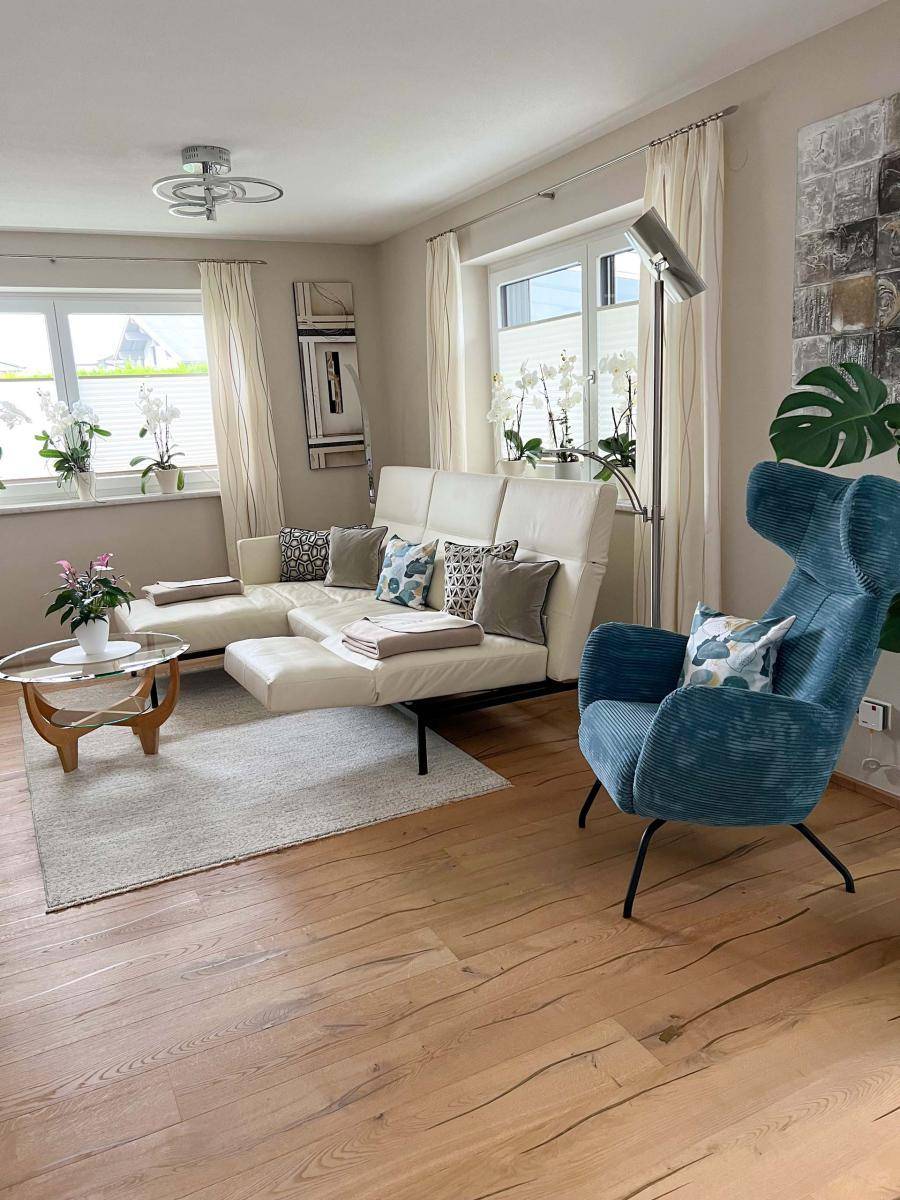 Gemütliches Wohnzimmer mit hellem Sofa, Holzboden und großen Fenstern für viel Tageslicht.