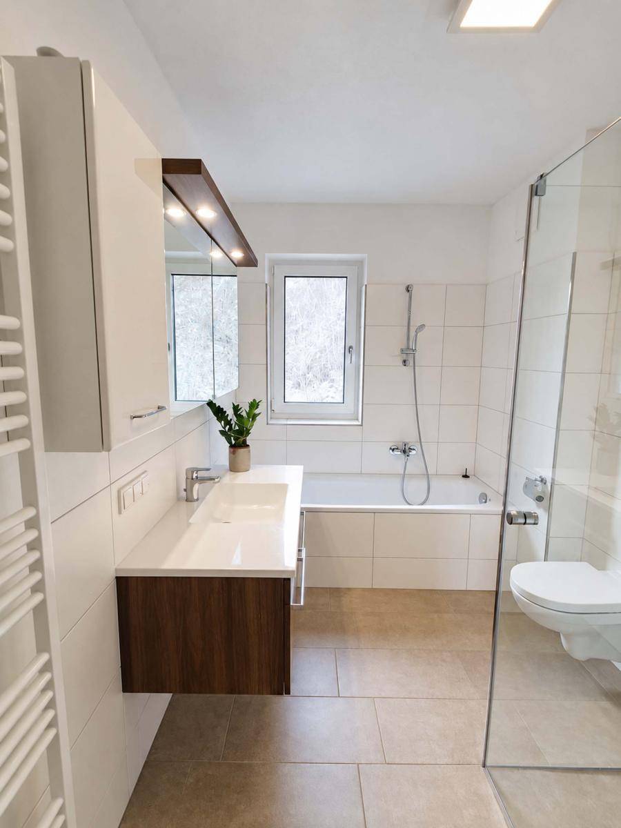 Modernes Badezimmer mit Badewanne, separater Dusche, Waschtisch und Fenster für natürliches Licht.