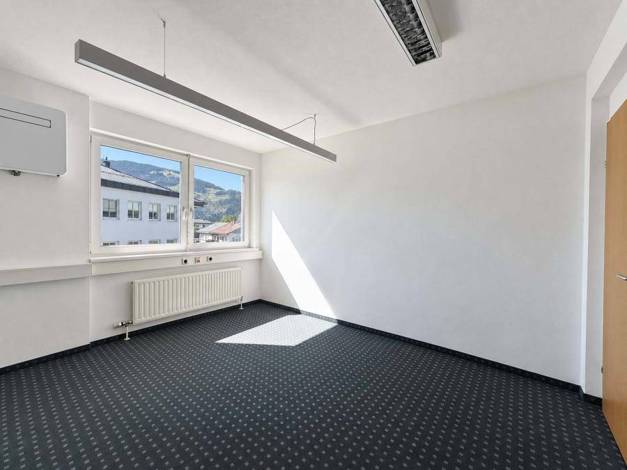Helles Büro mit dunklem Teppichboden, großem Fenster und Heizkörper, ideal für konzentriertes Arbeiten.