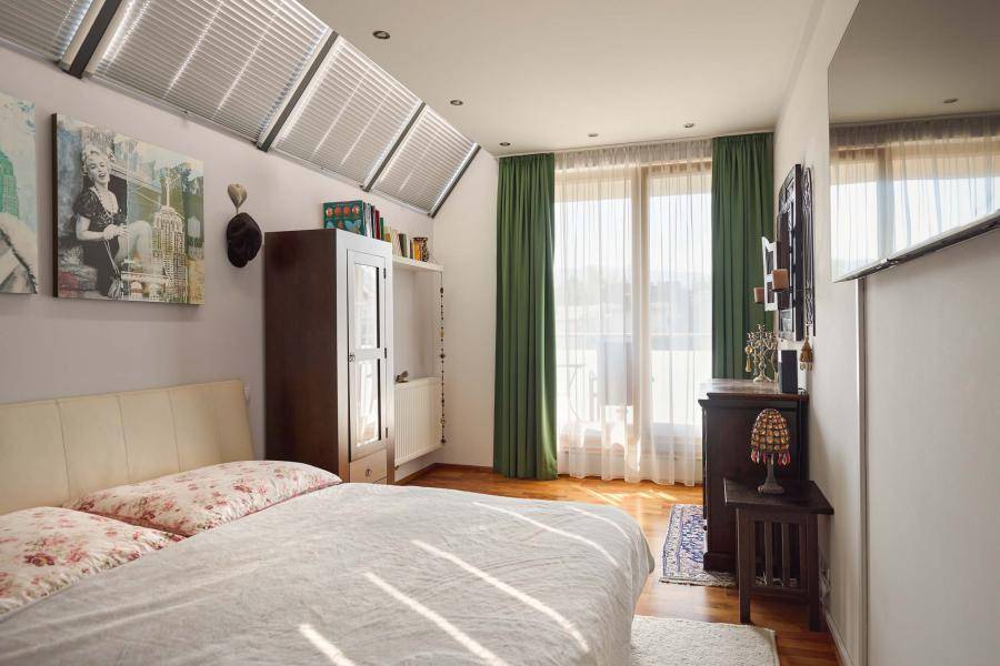 Helles Schlafzimmer mit Holzboden, Dachfenstern und Zugang zu einem Balkon.