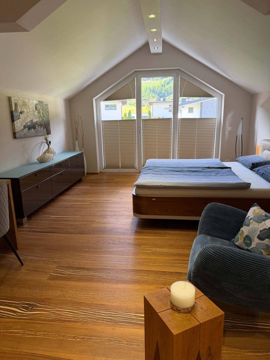 Helles Schlafzimmer mit Holzboden, großem Fenster und gemütlicher Sitzecke unter der Dachschräge.